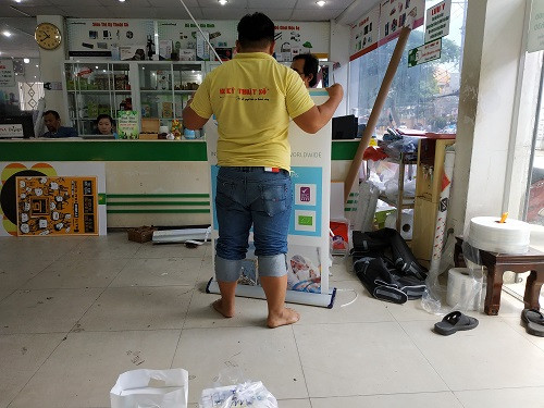 Nhân viên công ty in ấn lắp sẵn poster vào standee cuộn cho khách hàng